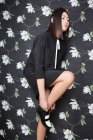 Hübsche Frau in schwarzem Kleid mit Schuhen auf floralem Hintergrund — Stockfoto