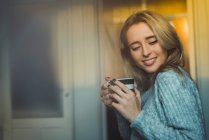Fröhliche junge blonde Frau entspannt mit Tasse zu Hause. — Stockfoto
