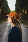 Jovem mulher de chapéu na ensolarada estrada da floresta — Fotografia de Stock