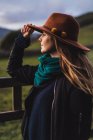 Donna sognante in piedi alla recinzione sul campo e cappello toccante — Foto stock