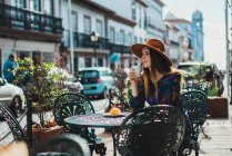Mulher sorridente sentada com xícara no terraço do café e olhando para o lado — Fotografia de Stock
