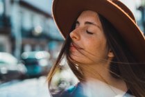 Pretty sensual woman in hat posing with eyes closed on street. — Stock Photo