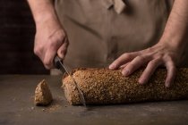 Средняя часть мужских рук режет свежеиспеченный хлеб — стоковое фото