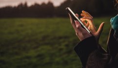 Обрезать женские руки просматривая смартфон на зеленом поле сельской местности — стоковое фото