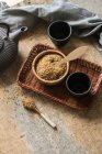 Прямо над видом на чашу, полную коричневого сахара на плетеном подносе и чашки чая — стоковое фото