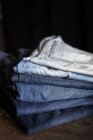 Stacked blue jeans pants on dark table. — Stock Photo