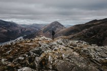 Vista laterale di escursionista in piedi su una collina rocciosa nella giornata nuvolosa . — Foto stock