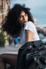 Young curly brunette woman posing in city and looking away. — Stock Photo