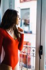 Brunette woman in red dressleaning on window — Stock Photo