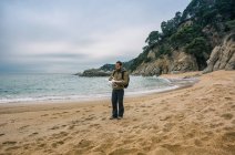 Uomo con zaino in piedi sulla spiaggia e drone di prova in aria — Foto stock
