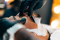 Парикмахерские руки в защитных перчатках бритья бороды клиента — стоковое фото