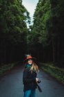 Joyeux jeune femme debout avec caméra sur la route asphaltée dans la forêt . — Photo de stock