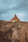 Vue sur colline sablonneuse et petite maison sur terrain sec par temps nuageux . — Photo de stock
