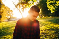 Junger Mann steht bei sonnigem Tag auf grünem Rasen im Park und blickt nach unten — Stockfoto