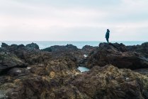 Frau steht an bewölktem Tag auf Steinen über dem Meer — Stockfoto