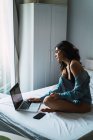 Brünette Frau sitzt auf Bett und benutzt Laptop zu Hause — Stockfoto