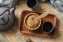 Diretamente acima vista de tigela cheia de açúcar mascavo na bandeja de vime e xícaras de chá — Fotografia de Stock