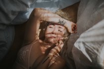 Portrait of blonde woman in bed with curtain shadow on face — Stock Photo