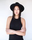 Young stylish woman in hat posing with arms crossed on white background. — Stock Photo
