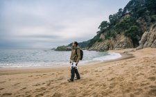 Чоловік з рюкзаком, що йде на пляжі з безпілотником в руці — стокове фото