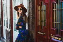Cheerful stylish woman in hat leaning on doorway at street — Stock Photo