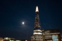 Rascacielos brillante en el distrito moderno contra el cielo nocturno con la luna . - foto de stock