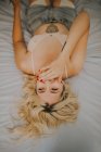 Von oben junge fröhliche blonde Frau lachend und auf dem Bett liegend. — Stockfoto