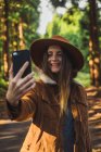 Cheerful young woman taking selfie in sunlit  forest. — Stock Photo