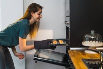 Mujer poniendo probar con galletas en el horno en la cocina - foto de stock