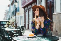 Усміхнена жінка позує з чашкою за столом у кафе — стокове фото