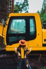 Elegante donna in cappello e poncho che mostra il gesto rock and roll sullo sfondo del trattore . — Foto stock