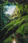 Vista lateral do turista em pé na caverna coberta com musgo e olhando para cima . — Fotografia de Stock