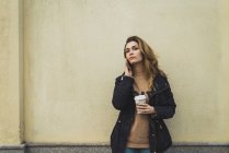 Mulher posando com smartphone e takeaway café por parede — Fotografia de Stock