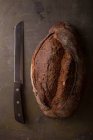 Свіжоспечений хліб і ніж на коричневому столі — стокове фото