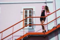 Vista lateral da jovem mulher atraente posando em escadas na rua . — Fotografia de Stock