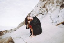 Stylish brunette girl sitting on shore rocks — Stock Photo