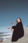 Молода жінка в чорному пальто на узбережжі над чистим небом — стокове фото