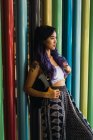 Молодая женщина с фиолетовыми волосами опирается на красочные колонны и смотрит в сторону . — стоковое фото