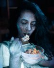 Жінка з блискітками на обличчі їсть зернові — стокове фото