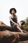 Sensual woman in hat sitting on log pile — Stock Photo