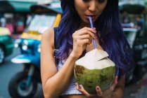 Erntefrau mit lila Haaren trinkt auf der Straße Kokosnuss mit Stroh. — Stockfoto