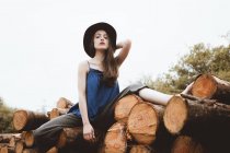 Sensual morena mulher de chapéu sentado na pilha de log — Fotografia de Stock