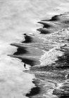 Вид с воздуха на неузнаваемого туриста, идущего по песчаному берегу волнистого моря . — стоковое фото