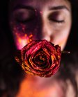Junge hübsche Frau mit glitzernden und fluoreszierenden roten Rosen im Mund. — Stockfoto