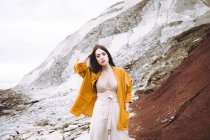 Bruna ragazza in reggiseno e giacca gialla posa sopra scogliera rocciosa — Foto stock