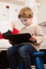 Loira menino sentado em casa e brincando com tablet — Fotografia de Stock