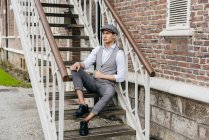 Веселый человек в винтажной одежде и кепке сидит на лестнице — стоковое фото