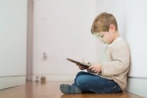Вид збоку блондинки хлопчик грає з планшетом, сидячи на підлозі — стокове фото