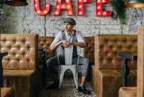 Mann in Vintage-Klamotten posiert auf Stuhl im Café und schaut zur Seite — Stockfoto