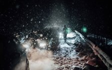 Pessoa irreconhecível de pé ao longo de carros presos na estrada na neve na noite de inverno . — Fotografia de Stock